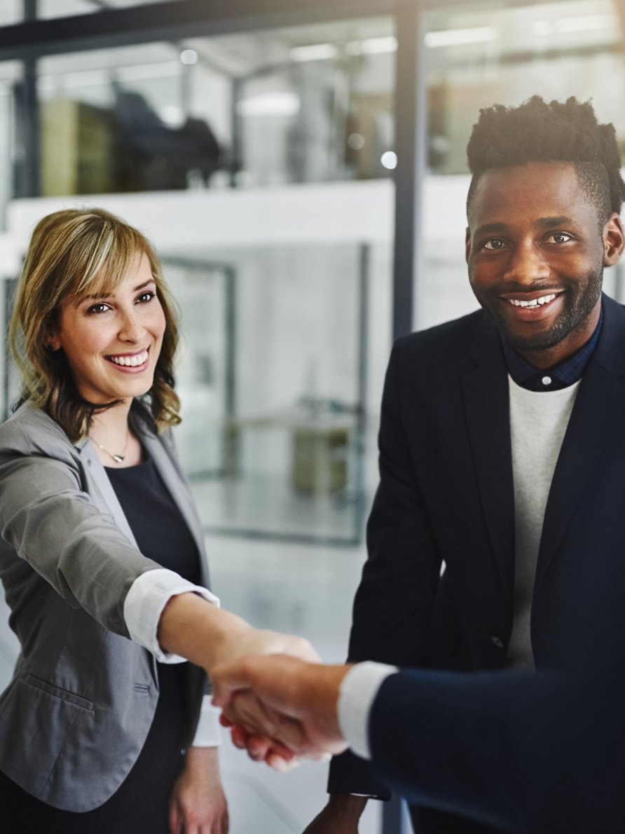Man and woman in business attire shaking a hand and smiling