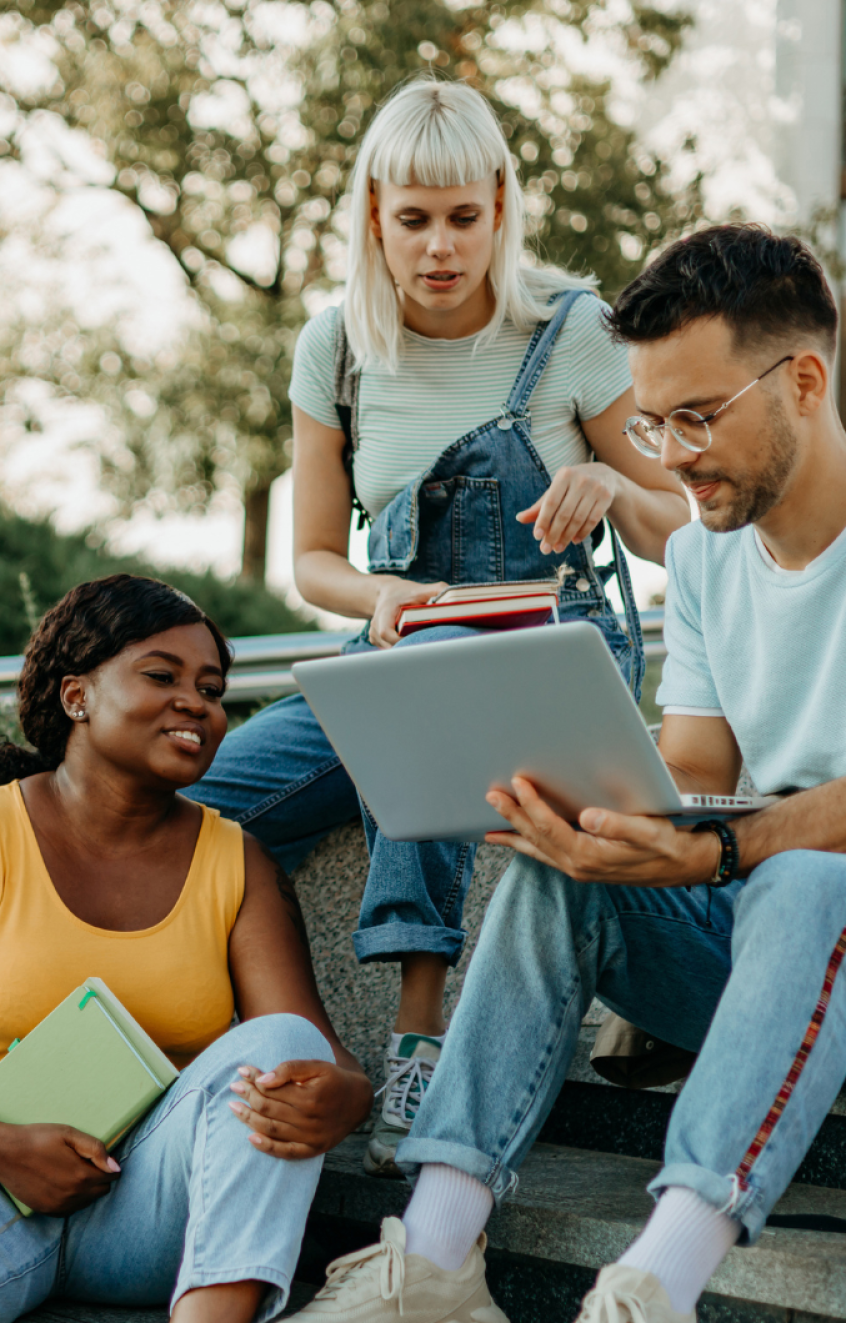 3 college students sitting outside, looking at a laptop.