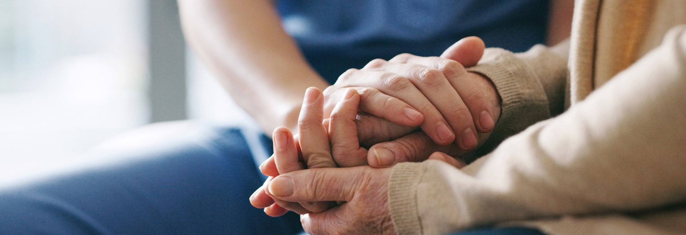 Close up photo of of an older adult woman holding hands with a nurse.